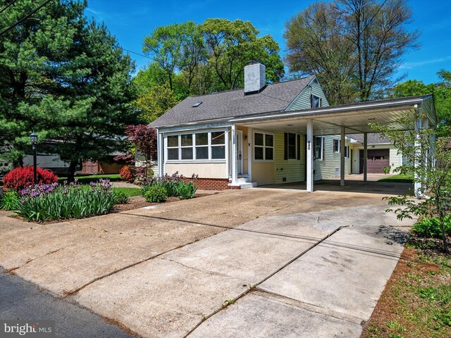 view of front facade with roof with shingles, entry steps, a chimney, a carport, and driveway