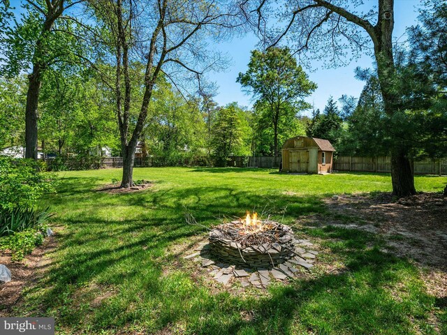view of yard with an outdoor structure, a fenced backyard, a fire pit, and a storage shed