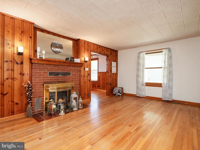 living area featuring visible vents, a brick fireplace, wood walls, baseboards, and wood-type flooring