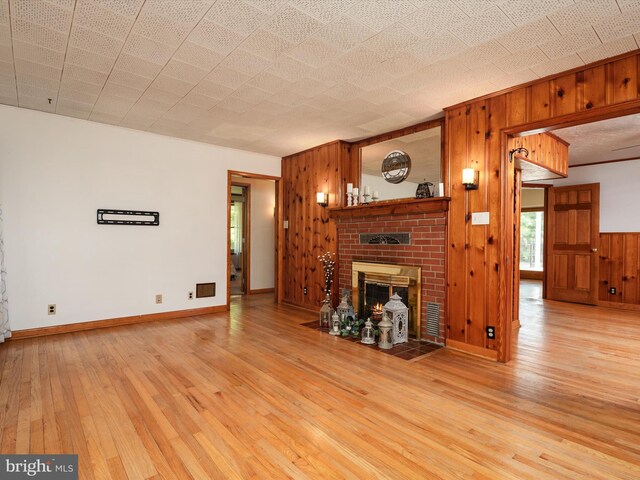 unfurnished living room featuring visible vents, wood walls, a fireplace, baseboards, and light wood finished floors