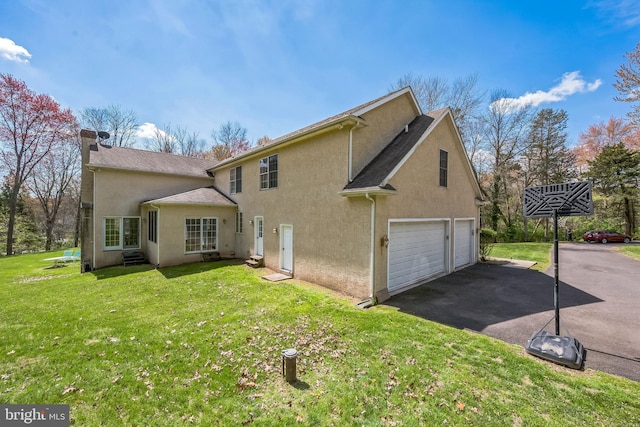 back of property with a lawn, a shingled roof, stucco siding, and aphalt driveway