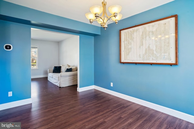spare room with baseboards, wood finished floors, and an inviting chandelier