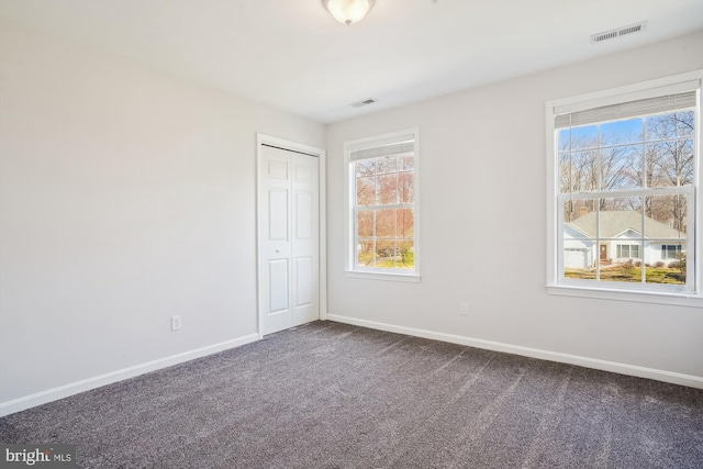 unfurnished bedroom with dark colored carpet, visible vents, and baseboards