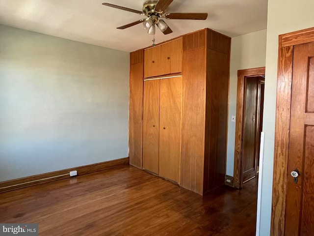 unfurnished bedroom with a closet, baseboards, dark wood-type flooring, and ceiling fan