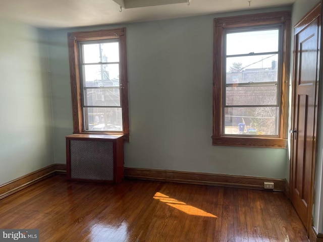 empty room featuring baseboards, radiator, and hardwood / wood-style flooring
