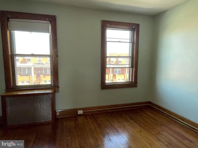 empty room featuring radiator, wood finished floors, and baseboards