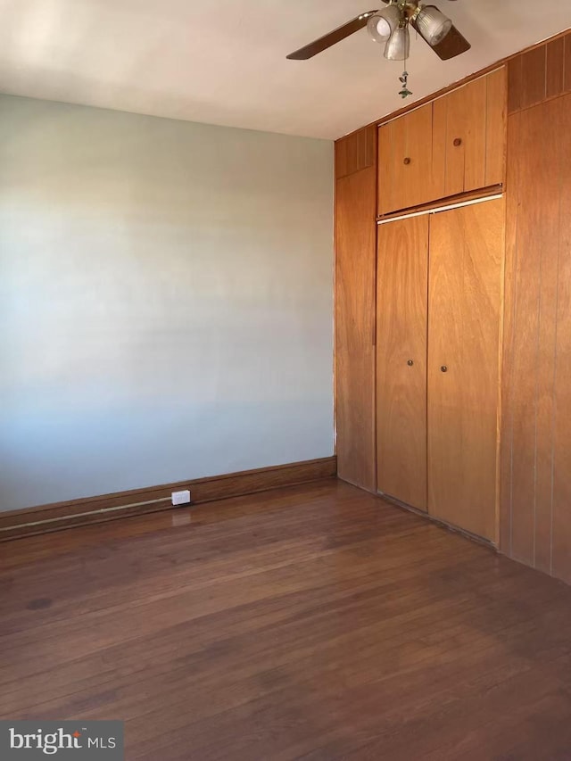 unfurnished bedroom featuring a closet, baseboards, wood finished floors, and a ceiling fan