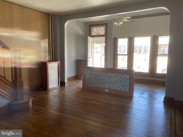 unfurnished living room featuring arched walkways, baseboards, ceiling fan, and wood finished floors