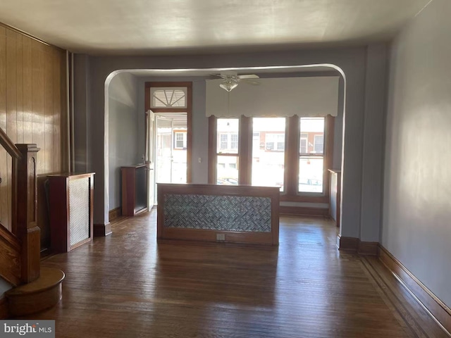 unfurnished living room featuring ceiling fan, baseboards, arched walkways, and dark wood finished floors