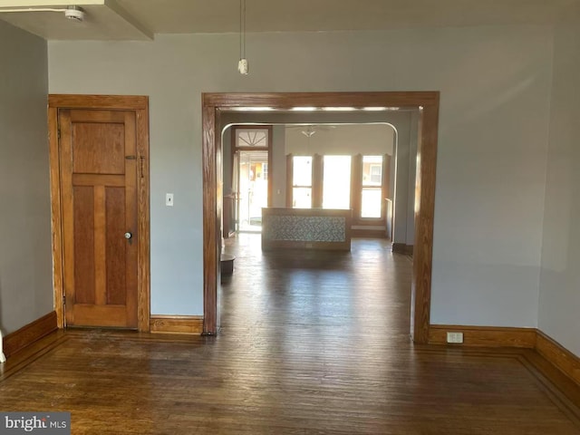 hall with baseboards, dark wood-style flooring, and arched walkways