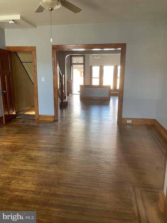 unfurnished room with arched walkways, baseboards, dark wood-style flooring, and ceiling fan