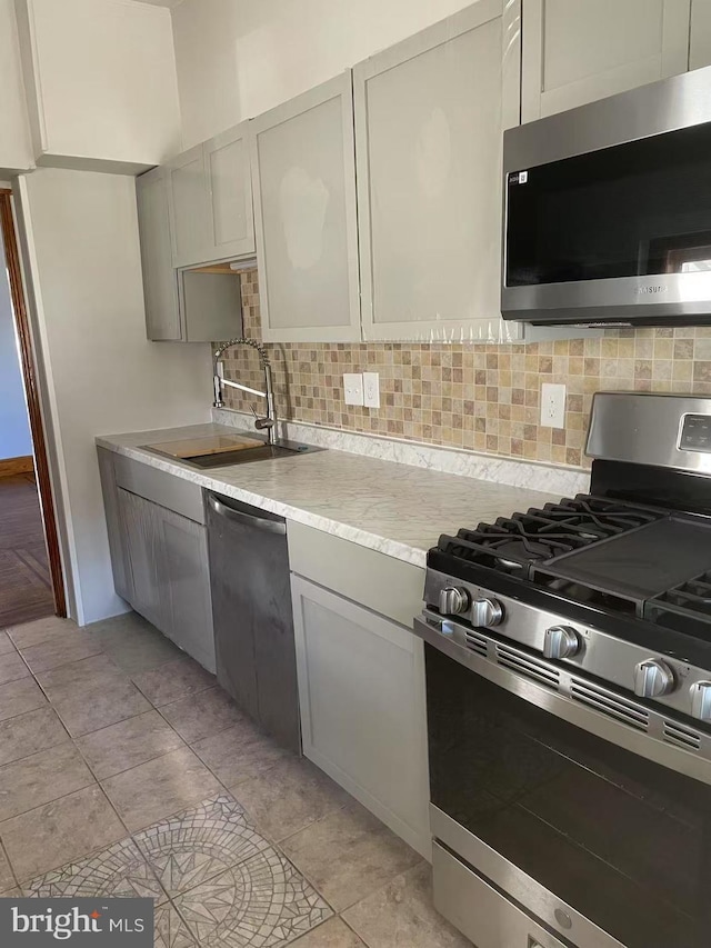 kitchen with gray cabinetry, a sink, backsplash, appliances with stainless steel finishes, and light countertops