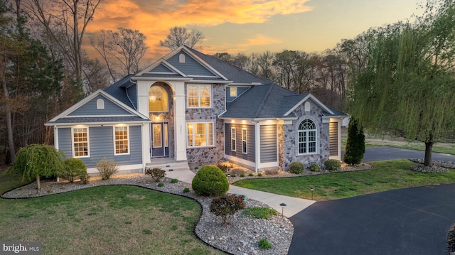 view of front of property with a shingled roof, stone siding, and a front lawn