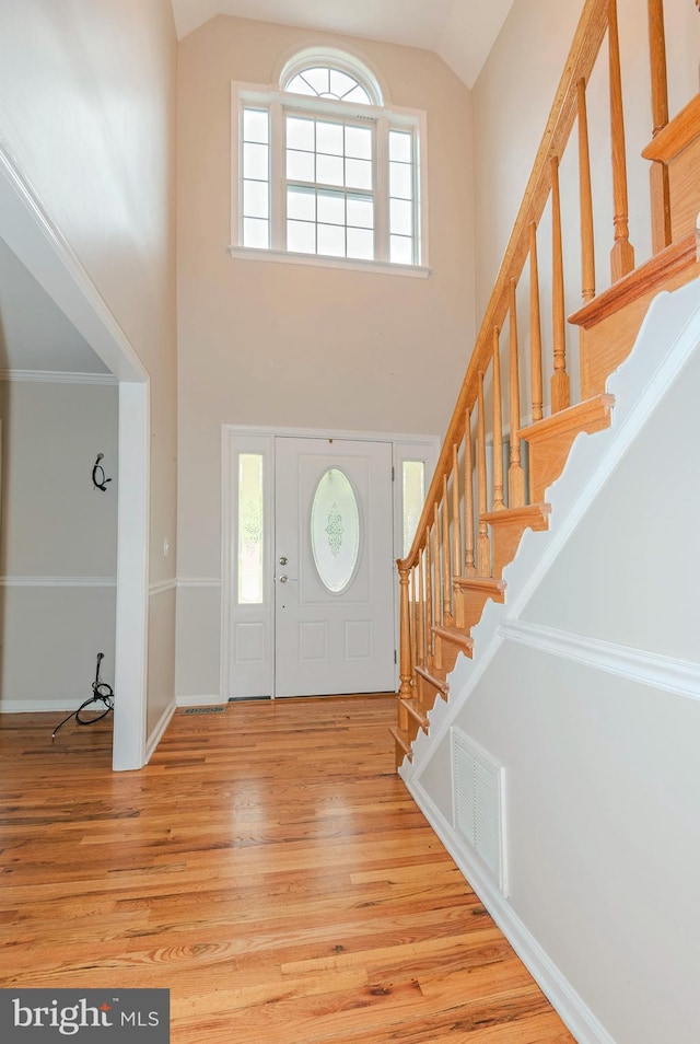 foyer entrance featuring stairs, visible vents, high vaulted ceiling, and wood finished floors