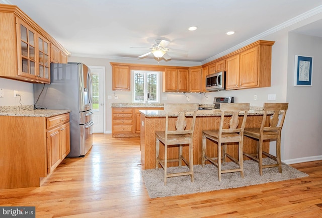 kitchen with light wood-style flooring, a peninsula, appliances with stainless steel finishes, and glass insert cabinets