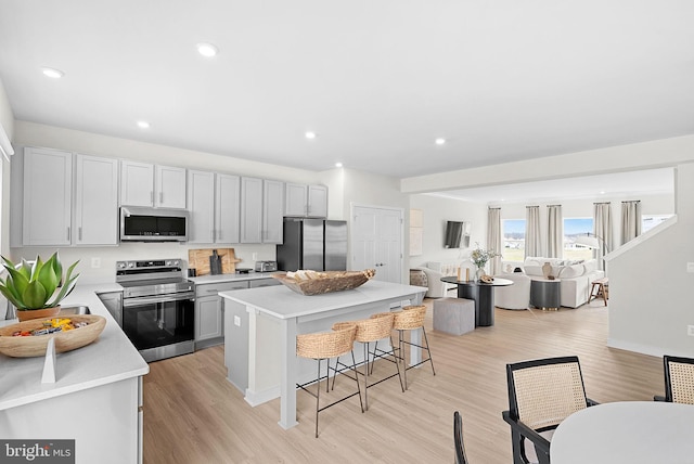 kitchen with open floor plan, light countertops, a kitchen island, a breakfast bar area, and appliances with stainless steel finishes