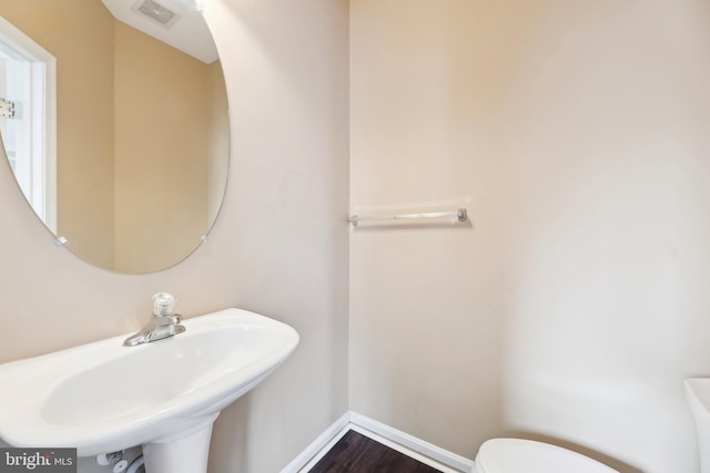 half bathroom with visible vents, toilet, wood finished floors, a sink, and baseboards