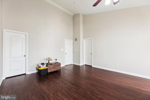 empty room with baseboards, a high ceiling, a ceiling fan, visible vents, and dark wood finished floors