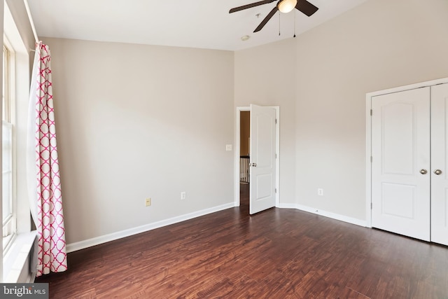 unfurnished bedroom with dark wood-type flooring, a closet, a ceiling fan, a high ceiling, and baseboards