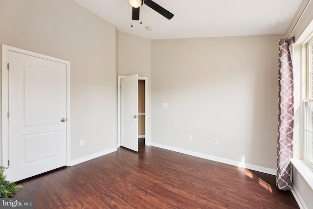 unfurnished bedroom featuring dark wood-type flooring, baseboards, a ceiling fan, and lofted ceiling