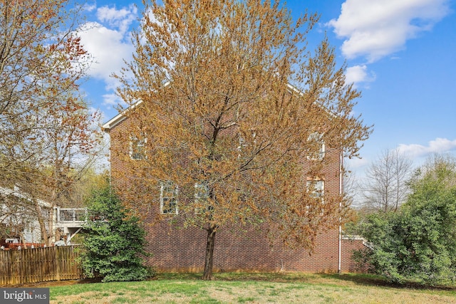 view of side of home with a yard, brick siding, and fence