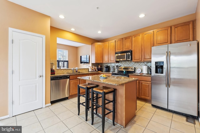 kitchen with light tile patterned floors, a sink, appliances with stainless steel finishes, backsplash, and a kitchen island