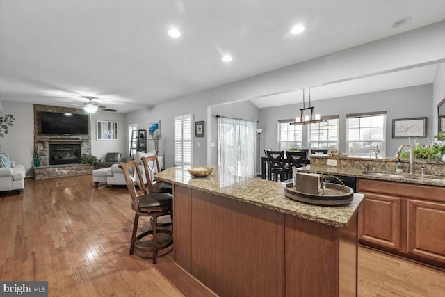 kitchen featuring a sink, a kitchen breakfast bar, a fireplace, and light stone countertops