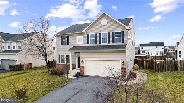 traditional-style house featuring a front yard, fence, driveway, an attached garage, and brick siding