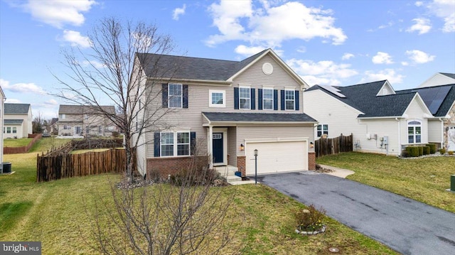 traditional-style home featuring driveway, fence, a front yard, an attached garage, and brick siding