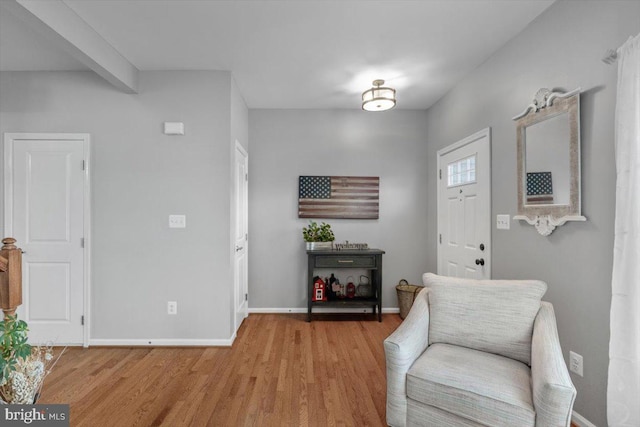living area with beamed ceiling, baseboards, and light wood-style flooring