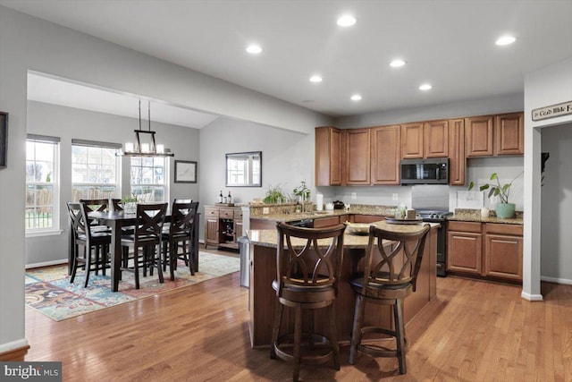 kitchen featuring stainless steel microwave, light stone countertops, light wood-type flooring, and range
