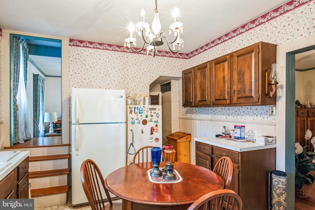 dining area with a wainscoted wall, an inviting chandelier, and wallpapered walls