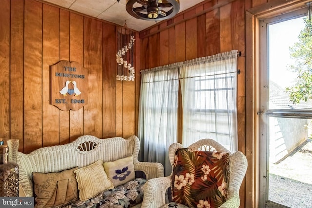 sitting room with wood walls, a healthy amount of sunlight, and a ceiling fan