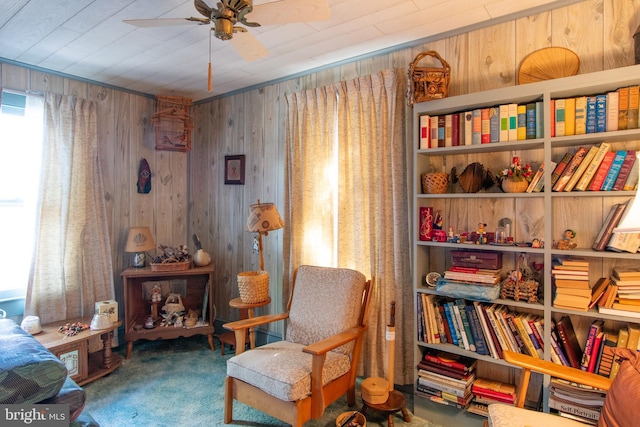living area featuring ceiling fan, wood walls, and carpet