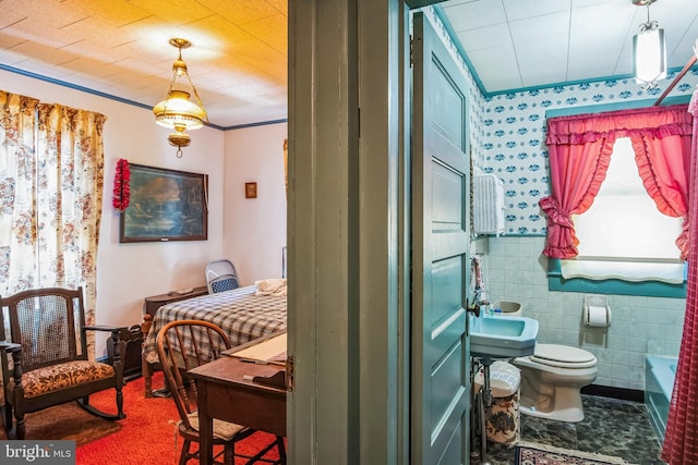 bathroom featuring wallpapered walls, a wainscoted wall, toilet, a tub to relax in, and tile walls