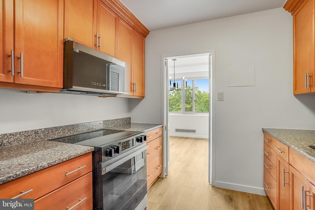 4101 Cathedral Ave NW Unit 1104, Washington, DC 20016 - kitchen with stainless steel microwave, range with electric cooktop, light wood finished floors, stone countertops, and brown cabinetry