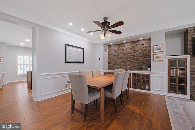 dining space featuring a decorative wall, ornamental molding, a ceiling fan, a wainscoted wall, and hardwood / wood-style floors