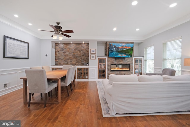 living area featuring crown molding, ceiling fan, a glass covered fireplace, visible vents, and hardwood / wood-style flooring