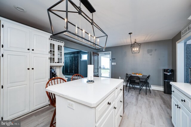 kitchen featuring a kitchen bar, a baseboard heating unit, a center island, light wood-style floors, and light countertops