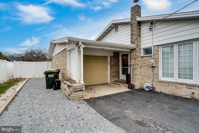 exterior space featuring an attached garage, fence, a chimney, stone siding, and driveway
