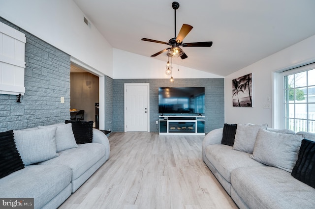 living room with visible vents, lofted ceiling, light wood-style flooring, ceiling fan, and a glass covered fireplace