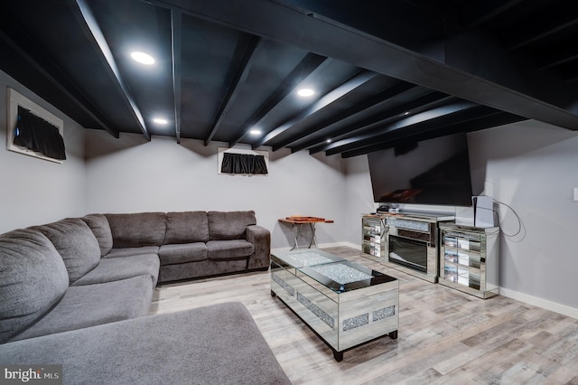 living area featuring a glass covered fireplace, beamed ceiling, baseboards, and wood finished floors