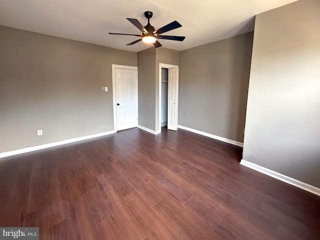 empty room with baseboards, ceiling fan, and dark wood-type flooring