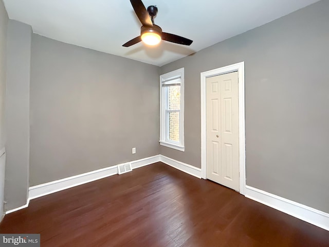 unfurnished bedroom featuring dark wood-style flooring, baseboards, a closet, and ceiling fan