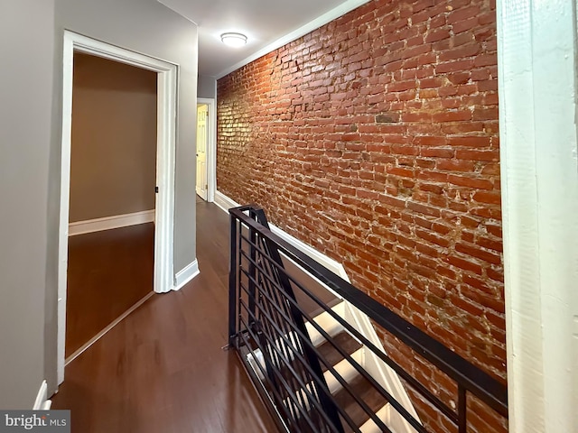 corridor featuring wood finished floors, brick wall, and baseboards