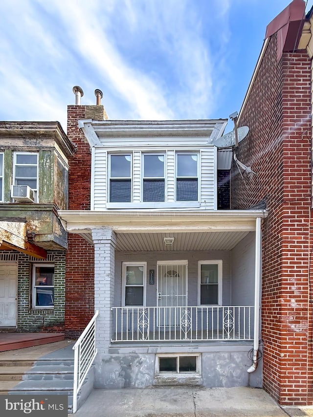 view of property featuring covered porch, brick siding, and cooling unit