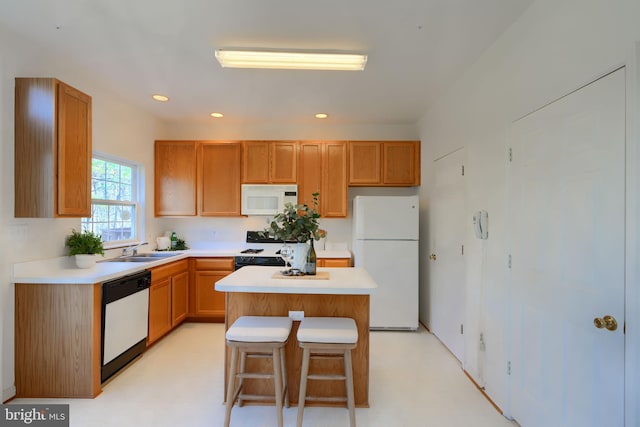 kitchen with a center island, a breakfast bar, light countertops, white appliances, and a sink