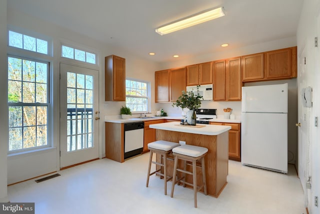 kitchen featuring white appliances, visible vents, a kitchen island, a sink, and light countertops