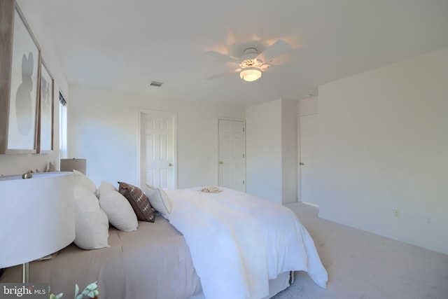 bedroom with visible vents, light colored carpet, and a ceiling fan