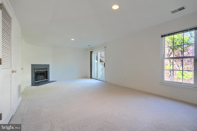unfurnished living room featuring visible vents, recessed lighting, a fireplace with flush hearth, and carpet floors